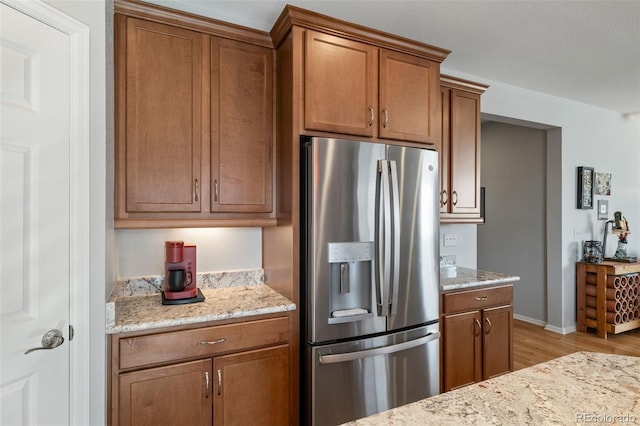 kitchen featuring stainless steel fridge with ice dispenser, baseboards, light stone counters, light wood-style flooring, and brown cabinets