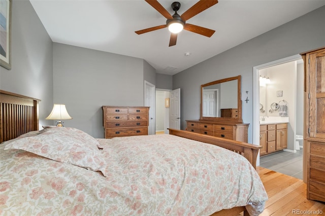bedroom featuring light wood finished floors, ensuite bath, and a ceiling fan