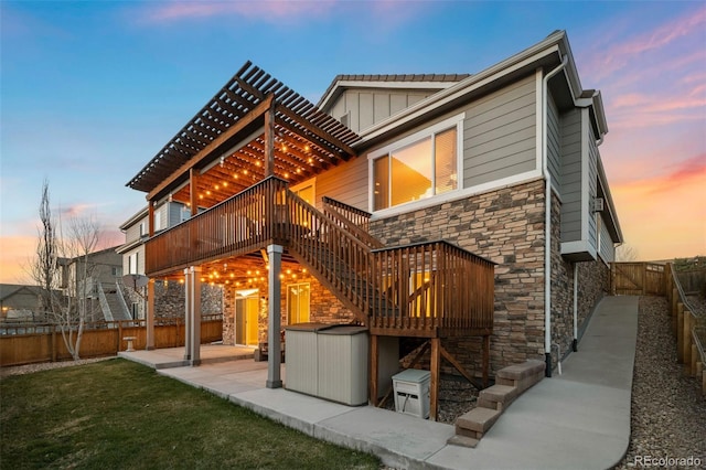 back of property with a deck, stone siding, board and batten siding, a fenced backyard, and a patio