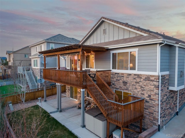 back of property at dusk featuring a deck, board and batten siding, stone siding, and stairs