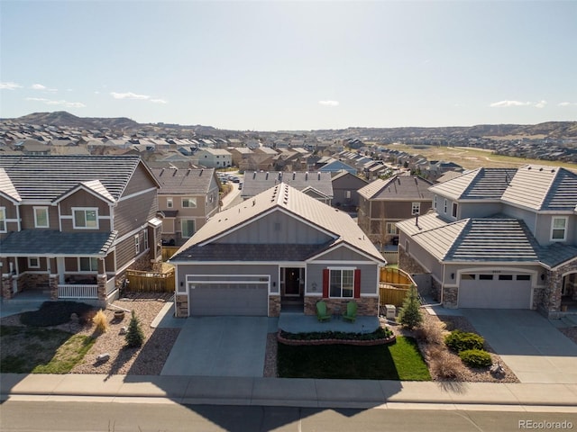 view of front of house featuring a garage, stone siding, fence, driveway, and a residential view
