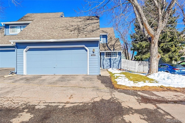 view of front of property with an attached garage, a shingled roof, and fence