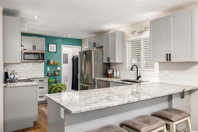 kitchen featuring appliances with stainless steel finishes, sink, kitchen peninsula, a breakfast bar, and light stone counters