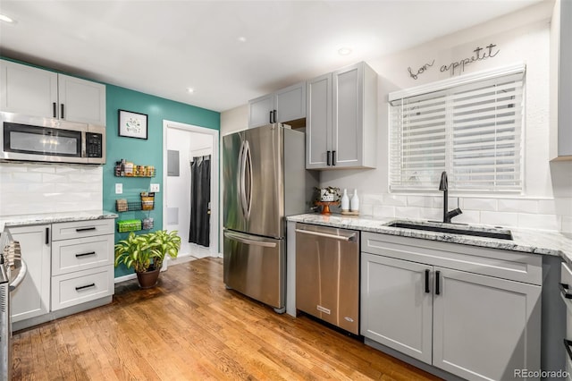 kitchen featuring appliances with stainless steel finishes, decorative backsplash, sink, gray cabinets, and light hardwood / wood-style flooring