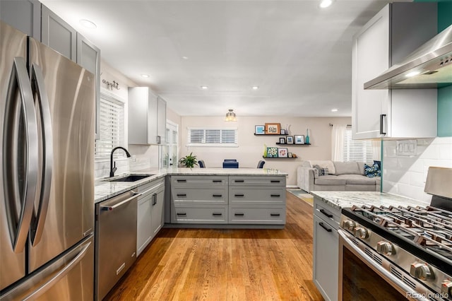 kitchen with sink, stainless steel appliances, wall chimney range hood, and gray cabinets