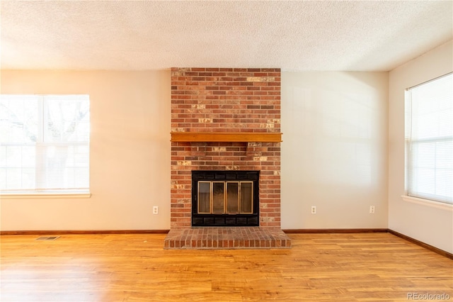 unfurnished living room featuring a brick fireplace, light wood-type flooring, and a textured ceiling