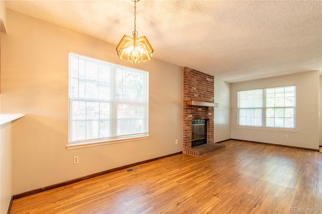 unfurnished living room featuring an inviting chandelier, wood-type flooring, a brick fireplace, and a textured ceiling