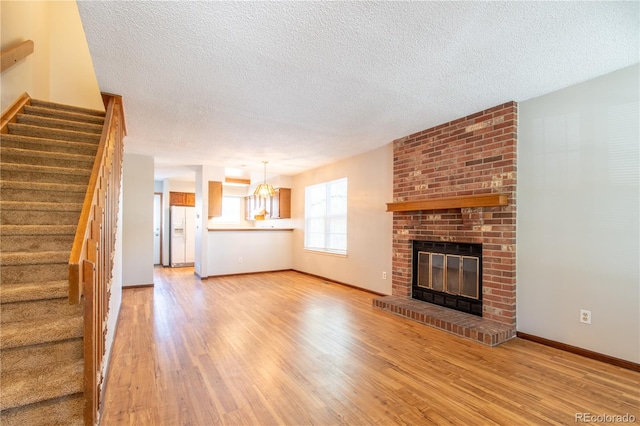 unfurnished living room featuring a fireplace, an inviting chandelier, light hardwood / wood-style floors, and a textured ceiling