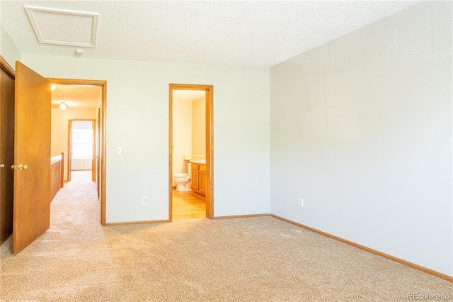 unfurnished bedroom featuring light carpet, ensuite bathroom, and a textured ceiling