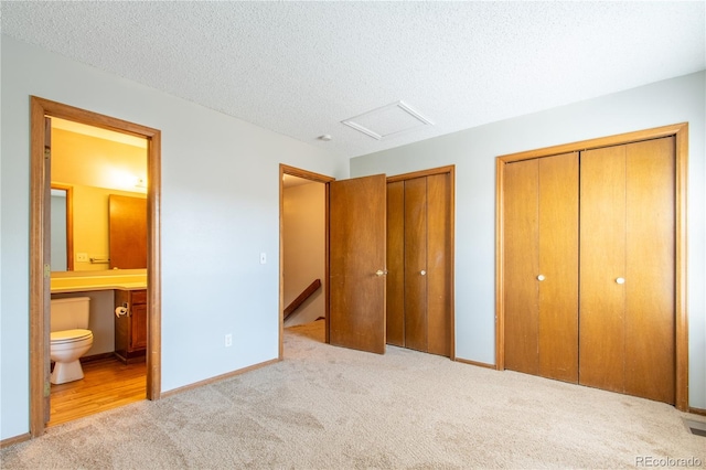 unfurnished bedroom featuring light carpet, a textured ceiling, two closets, and ensuite bathroom