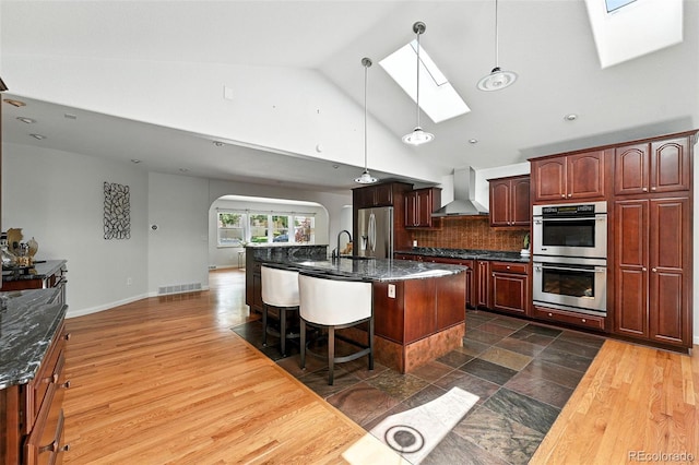 3608 S Newport Way, Denver, CO 80237 - kitchen with stainless steel appliances, a skylight, wall chimney range hood, arched walkways, and an island with sink
