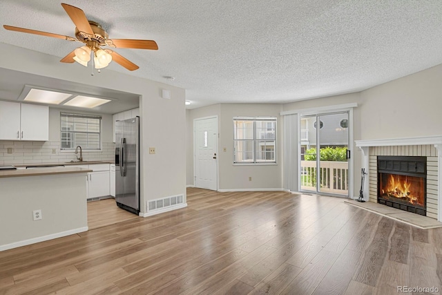 unfurnished living room featuring a ceiling fan, a textured ceiling, light wood-style flooring, a fireplace, and a sink