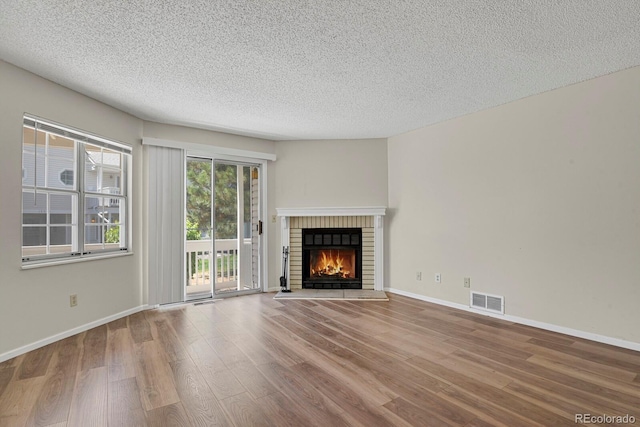 unfurnished living room with wood finished floors, a textured ceiling, a fireplace, and baseboards