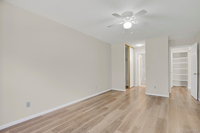 unfurnished room with a textured ceiling, light wood-type flooring, ceiling fan, and baseboards