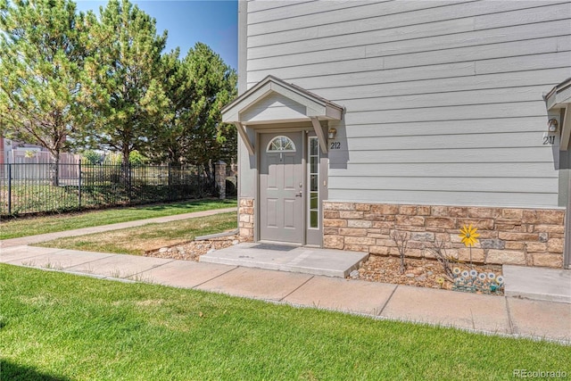 doorway to property featuring stone siding, a yard, and fence