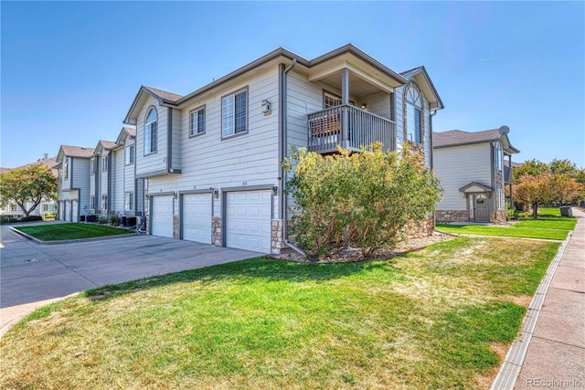 view of side of home with an attached garage, a balcony, driveway, stone siding, and a lawn