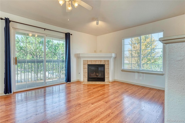 unfurnished living room with baseboards, a tile fireplace, wood finished floors, and a healthy amount of sunlight