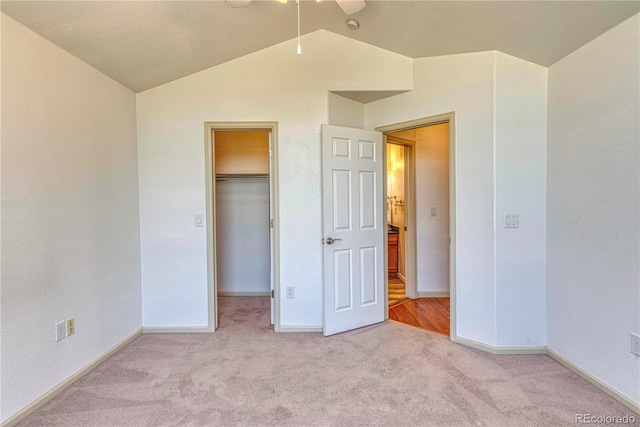 unfurnished bedroom with carpet floors, a walk in closet, vaulted ceiling, and baseboards