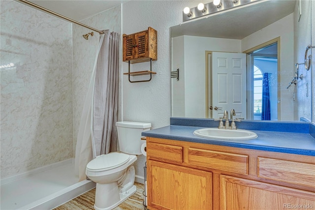 full bathroom with toilet, a stall shower, a textured wall, and vanity