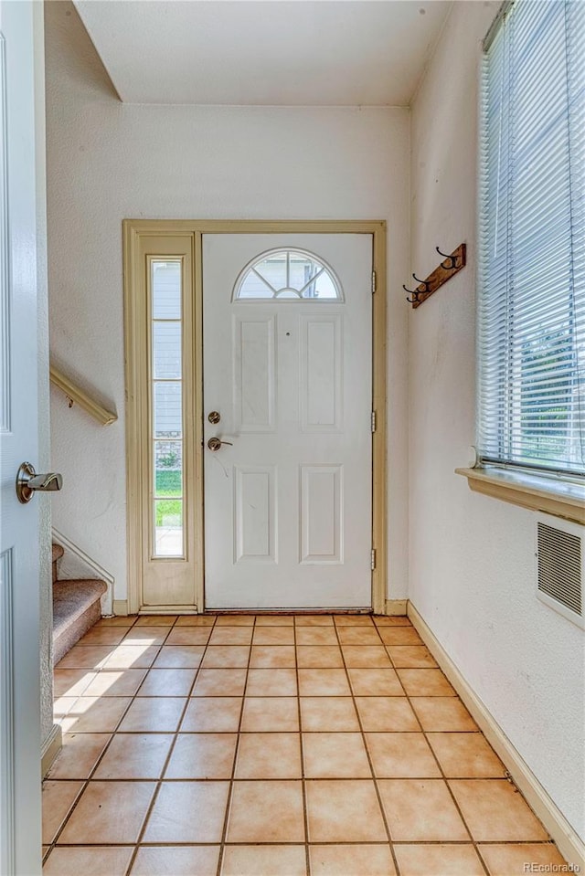 foyer with a healthy amount of sunlight, stairs, baseboards, and light tile patterned flooring