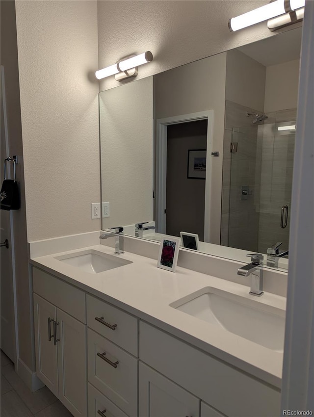 full bath featuring double vanity, a sink, a textured wall, and a shower stall