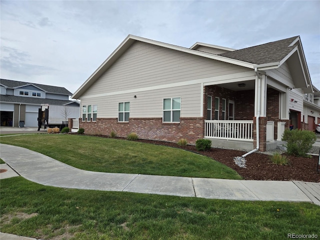 view of side of property with brick siding, a lawn, and covered porch
