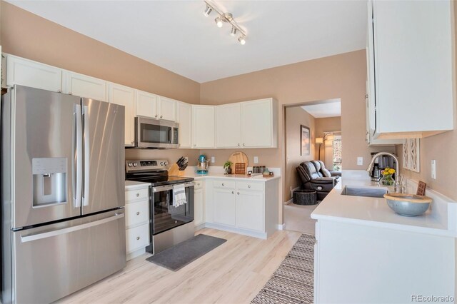 kitchen with a sink, light countertops, white cabinets, light wood-style floors, and stainless steel appliances