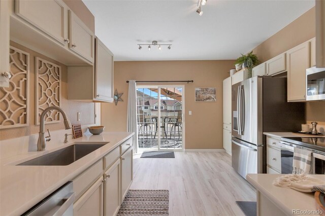 kitchen with appliances with stainless steel finishes, rail lighting, a sink, light countertops, and light wood-style flooring