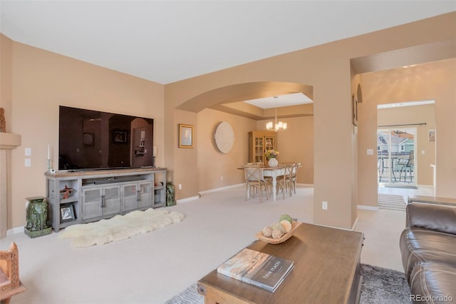 carpeted living area featuring baseboards, arched walkways, a tray ceiling, and a chandelier