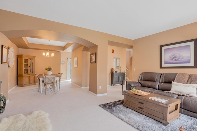 living room with baseboards, light colored carpet, a raised ceiling, arched walkways, and a notable chandelier