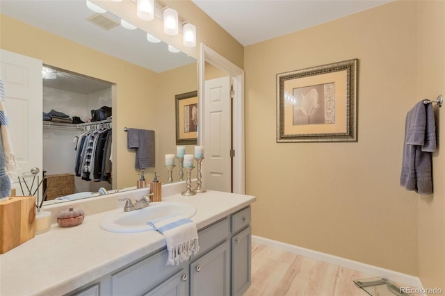 bathroom with a walk in closet, vanity, baseboards, wood finished floors, and visible vents