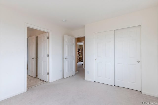 unfurnished bedroom featuring baseboards, a closet, and light colored carpet