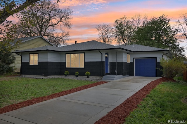 view of front facade with an attached garage, concrete driveway, a shingled roof, and a front lawn