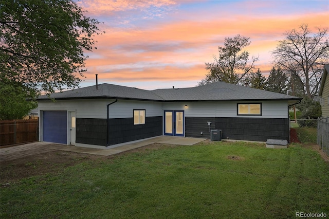 back of house featuring an attached garage, fence, a shingled roof, a yard, and driveway