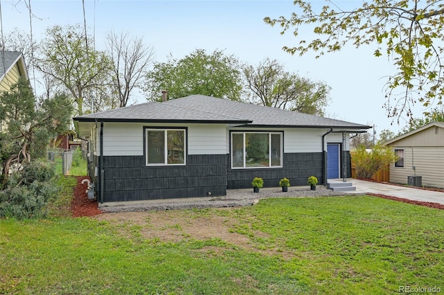 ranch-style house featuring a front lawn, a shingled roof, fence, and central AC