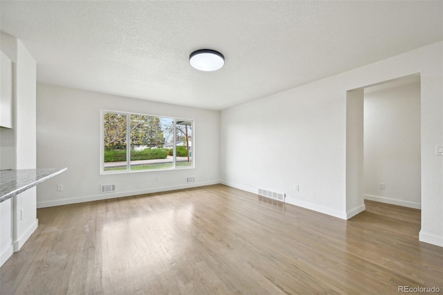 unfurnished living room with baseboards, visible vents, and wood finished floors