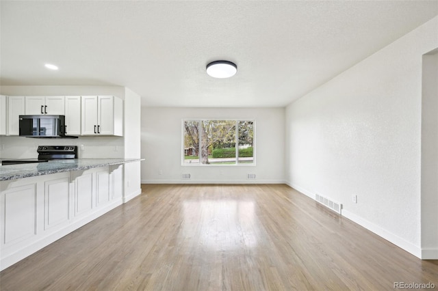 kitchen with light wood-type flooring, stainless steel electric range, light stone countertops, and visible vents