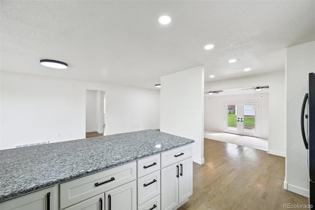 kitchen with french doors, light wood-type flooring, light stone counters, open floor plan, and white cabinets