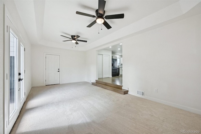 empty room featuring ceiling fan, light carpet, a tray ceiling, and visible vents