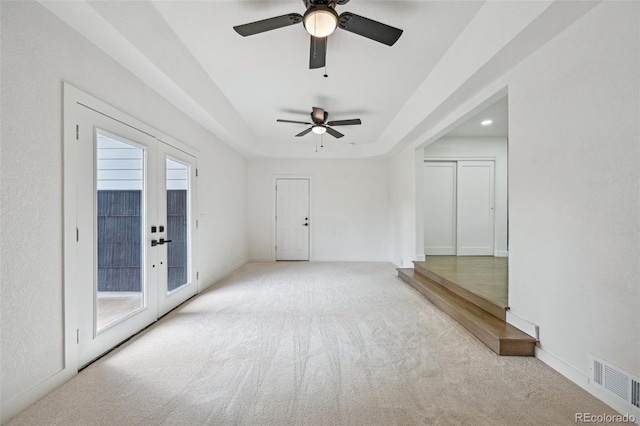 carpeted empty room featuring a tray ceiling, visible vents, french doors, and ceiling fan