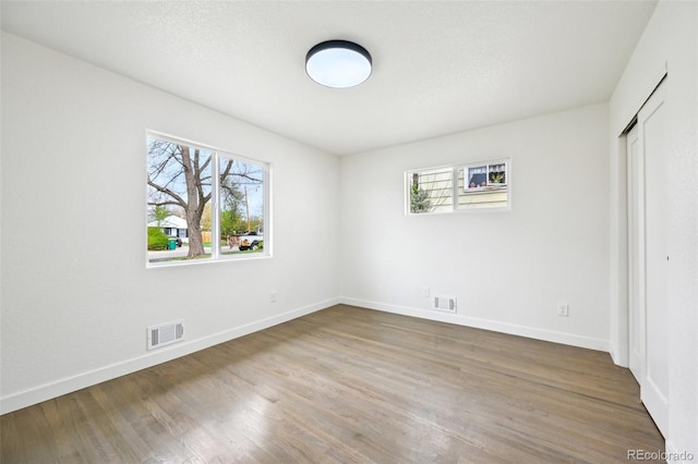 unfurnished bedroom featuring wood finished floors, visible vents, and multiple windows