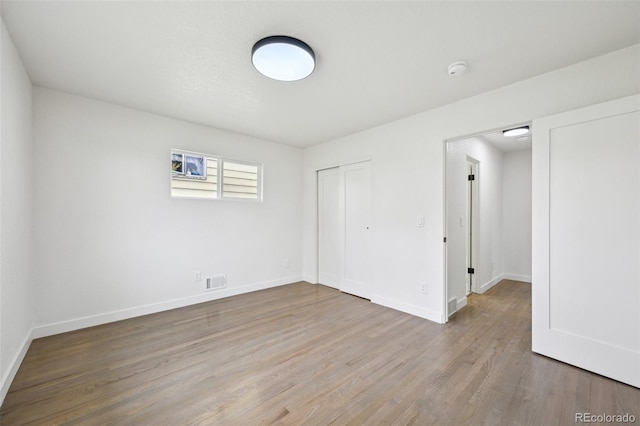 unfurnished bedroom featuring a closet, visible vents, wood finished floors, and baseboards