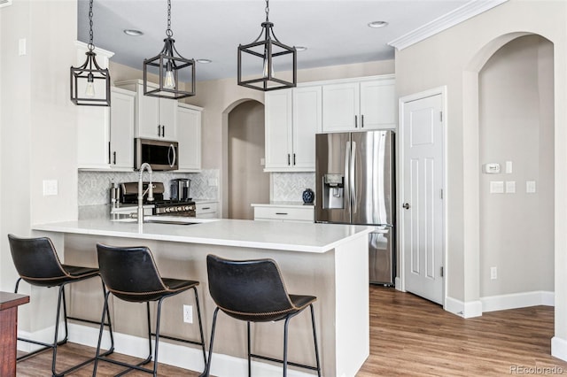 kitchen with appliances with stainless steel finishes, pendant lighting, white cabinets, light hardwood / wood-style floors, and kitchen peninsula