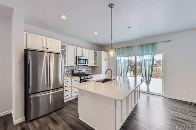 kitchen with pendant lighting, open shelves, appliances with stainless steel finishes, a kitchen island with sink, and a sink