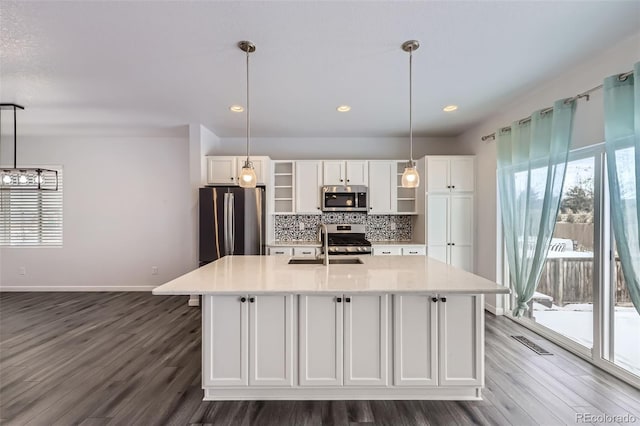 kitchen with decorative light fixtures, stainless steel appliances, white cabinetry, visible vents, and a center island with sink