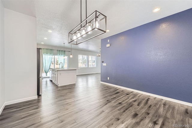 unfurnished living room featuring baseboards, dark wood finished floors, recessed lighting, a textured ceiling, and a sink