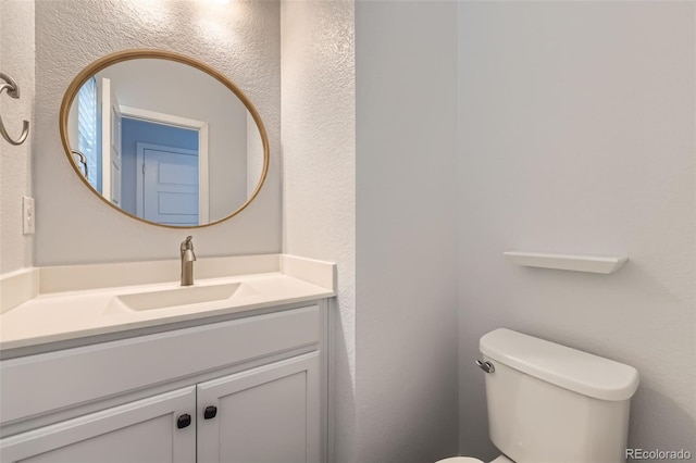 half bathroom featuring a textured wall, vanity, and toilet