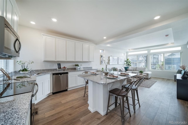 kitchen featuring stainless steel dishwasher, light wood-type flooring, light stone countertops, a kitchen breakfast bar, and white cabinets