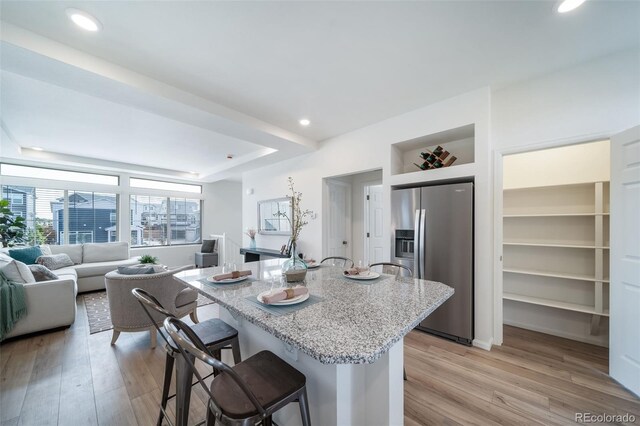 kitchen featuring a center island with sink, stainless steel fridge, a kitchen breakfast bar, light wood-type flooring, and built in features