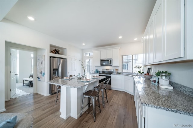 kitchen featuring white cabinets, appliances with stainless steel finishes, a kitchen island, a kitchen breakfast bar, and light stone counters